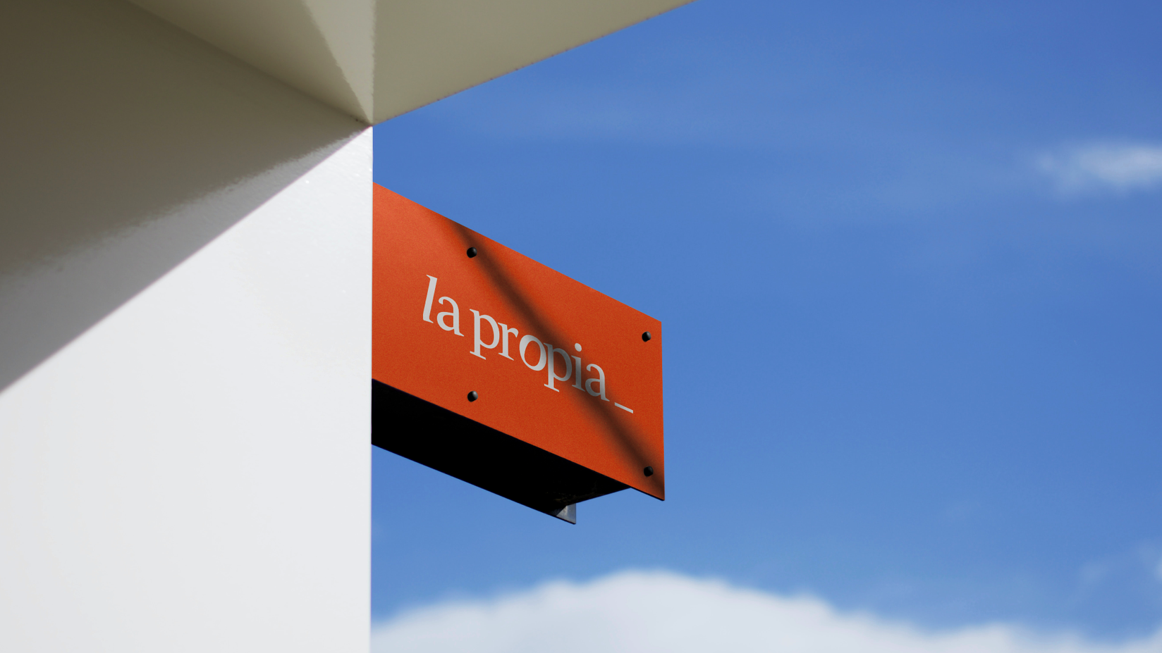 Rótulo rojo con el nombre 'la propia' colgado en la fachada de un edificio, destacando su identidad de marca