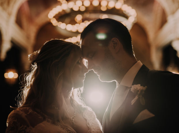 The bride and groom are in frame from chest upwards. Their foreheads touch and they have their eyes closed. Behind them are orbs of lights.