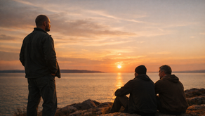 Tre män som sitter på en klippa och tittar ut mot havet och solnedgången