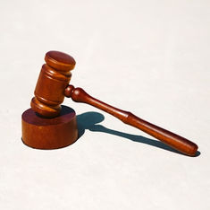 Wooden gavel resting on a sound block against a plain, light background. The image conveys a sense of justice or authority.