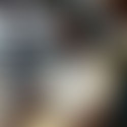 Smiling man in a white shirt sits in a room with wooden decor and plants. Soft lighting and a relaxed mood are evident.