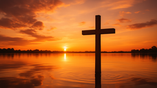 A wooden cross stands in calm water at sunset, with an orange sky and silhouetted trees. The mood is serene and reflective.