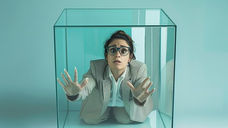 Person trapped inside glass box with hands pressed against the walls, representing the silencing of abuse survivors