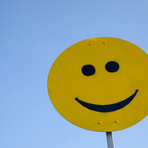 Yellow smiley face sign on a pole against a clear blue sky, conveying a happy and cheerful mood.