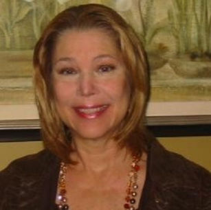 Debra Hodges with shoulder-length hair smiles, wearing a necklace with various beads. The background features a nature-themed painting.