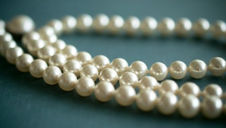 Strings of ivory pearls lie coiled on a muted teal surface, creating an elegant and classic visual contrast.