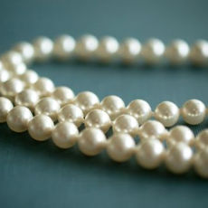 Strings of ivory pearls lie coiled on a muted teal surface, creating an elegant and classic visual contrast.