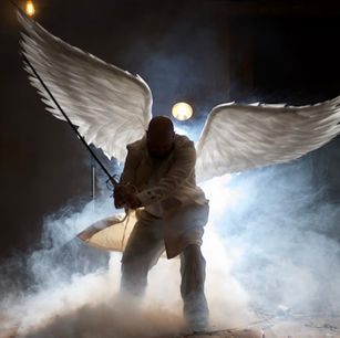 A person with large white wings and a sword kneels in a misty, dimly lit space, conveying a dramatic and mysterious mood.