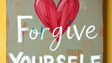 Wooden sign with a red heart and text reading "Forgive Yourself" in white. Set against a yellow wall, conveying a positive, encouraging mood.