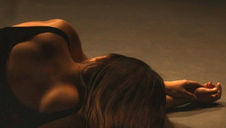 Woman lying on a dimly lit floor, facing away with her arm extended. Her hair cascades down, creating a calm, introspective mood.