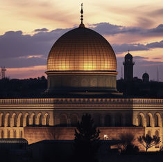 Illuminated golden-domed mosque at dusk, with a silhouetted city skyline and clouds in the background, illustrating the dome f the rock prophecy.