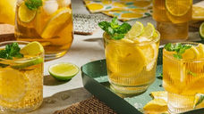 Glasses of iced tea with lemon, lime, and mint on a green tray in sunlight. Fresh, vibrant colors create a refreshing summer vibe.