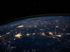 View of Earth from space at night showing illuminated cities. Stars twinkle in a dark sky. Calm, vast, and awe-inspiring scene.