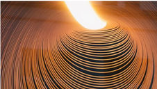 Abstract image of spiraling grooves with a bright light in the center. The pattern creates a hypnotic effect with warm orange tones.