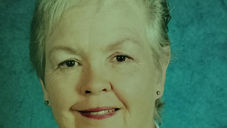 Woman with short gray hair smiling against a blue textured background, wearing a white shirt. The mood is calm and friendly.