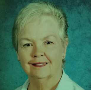 Woman with short gray hair smiling against a blue textured background, wearing a white shirt. The mood is calm and friendly.