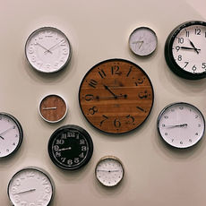 Various wall clocks with different designs and colors on a beige background. Largest clock is wooden. No visible text except clock numbers.