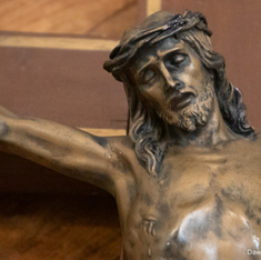 Close-up of a bronze crucifix, focusing on Christ's contemplative expression. Wooden cross background with warm tones.