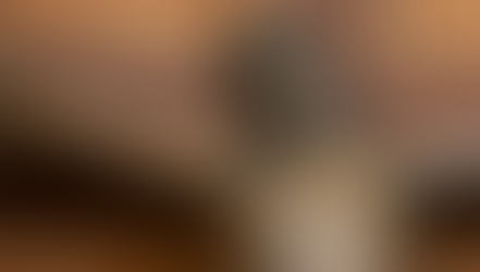 Close-up of a bronze crucifix, focusing on Christ's contemplative expression. Wooden cross background with warm tones.