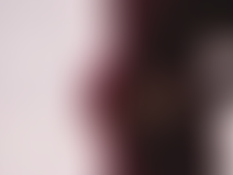 Pregnant woman in a burgundy dress holding her belly, standing against a sheer, light curtain. Light creates a peaceful, intimate mood.