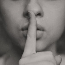 Close-up of a person holding a finger to their lips, signaling silence. Grayscale tones and soft focus create a calm, quiet mood.