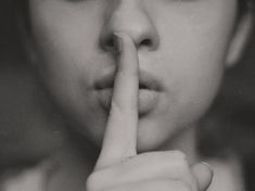 Close-up of a person holding a finger to their lips, signaling silence. Grayscale tones and soft focus create a calm, quiet mood.