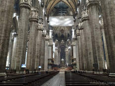 Majestic cathedral interior with towering stone columns and ornate arches. Rows of empty wooden pews lead to an intricate altar.