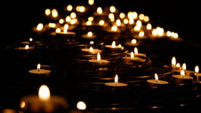 Numerous candles lit on spiral holders create a warm, serene glow against a dark background, evoking a peaceful, contemplative atmosphere.