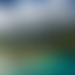 Aerial view of a lush, green mountain coastline meeting turquoise ocean waters under a partly cloudy sky, creating a serene and dramatic landscape.