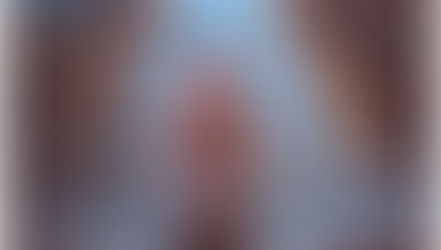 A man in gray shirt praying in an empty church, kneeling between pews. Soft light fills the room, creating a serene atmosphere.