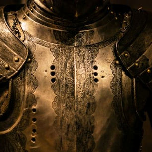 Close-up of ornate, dark metallic medieval armor with intricate engravings. The setting is dimly lit, highlighting the detailed craftsmanship.