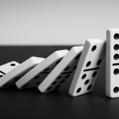Dominoes in a black and white setting, one standing upright while others fall in a line, conveying motion and balance.