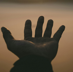 A dark hand reaches out against a soft, blurred golden background, evoking a sense of yearning or hope.