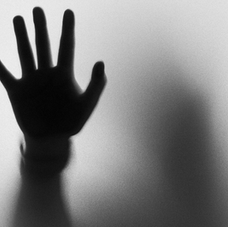 Silhouetted hand pressed against frosted glass, with a blurred figure behind it in a stark black-and-white eerie scene