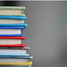 A stack of books with colorful spines (green, blue, red, yellow) against a plain gray background, creating a neat and vibrant mood.