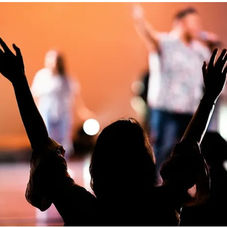 Silhouette of a person with raised hands at a concert. Blurred performers in the background. Bright stage lights create a vibrant atmosphere.