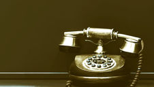 Vintage rotary phone with a wooden base and brass accents sits on a dark surface; dimly lit with a nostalgic, sepia tone.