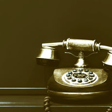Vintage rotary phone with a wooden base and brass accents sits on a dark surface; dimly lit with a nostalgic, sepia tone.