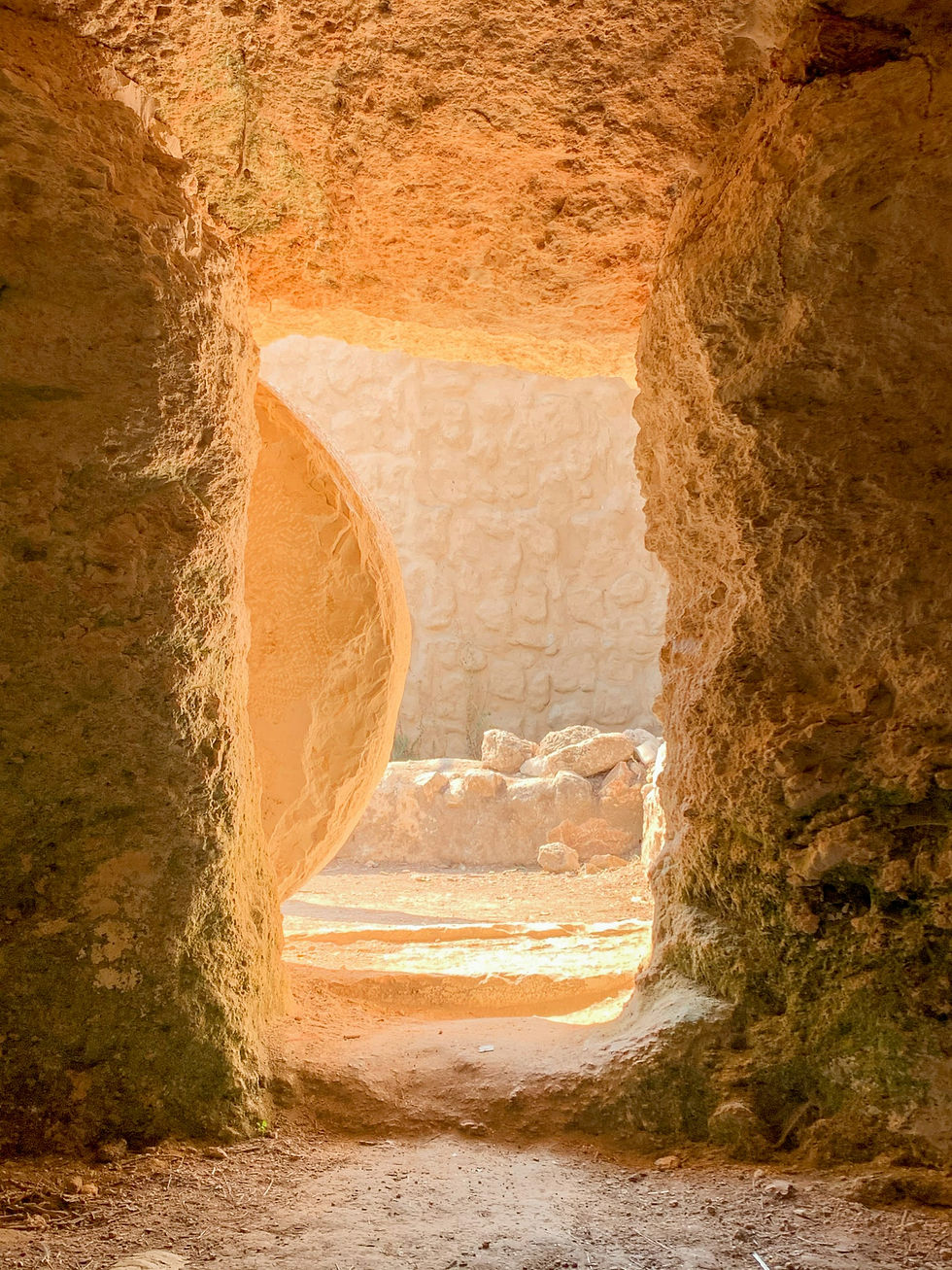 Sunlight illuminates an ancient stone tomb with a large round stone door, revealing a sandy, rocky interior and arched entrance.