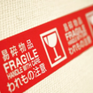 Red "Fragile, Handle with Care" tape with symbols and text in English and Japanese on a textured white background.