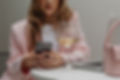 woman in a pink blazer at a table on her phone, drinking wine