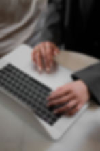 Hands typing on a laptop keyboard, wearing rings. The setting is a light-colored table. Mood is focused, with a neutral color palette.
