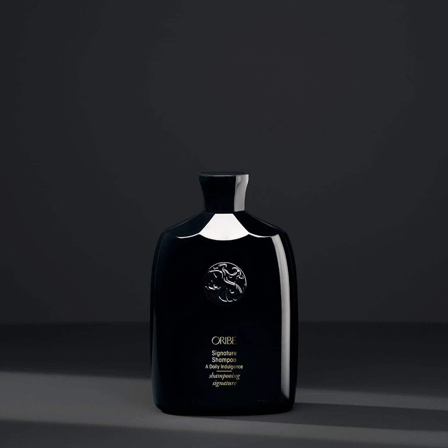 Elegant black bottle of Oribe Signature Shampoo with embossed logo—luxurious daily cleanser in a salon setting.