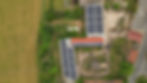 Luftaufnahme von Gewerbegebäuden mit Solaranlagen auf den Dächern, umgeben von grünen Bäumen und Grünflächen. Das Gebiet umfasst offene Felder, zusätzliche Gebäude und Straßen, die zu den Solargebäuden führen.