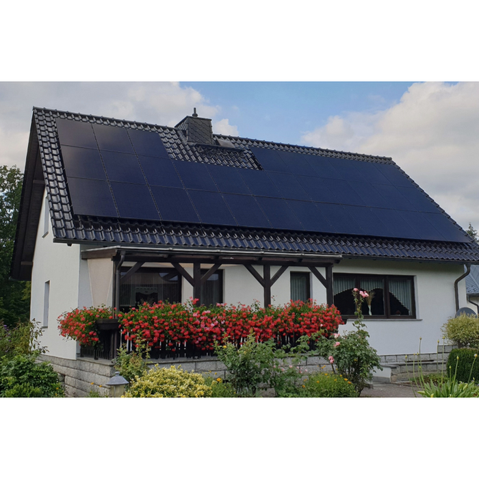 Privathaus mit weißen Wänden und schwarz gedecktem Dach, auf dem Solarmodule (12 kWp, 33 Solarmodule à 360 Wp) installiert sind.