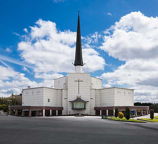 A large modern church with a tall spire and cloudy sky