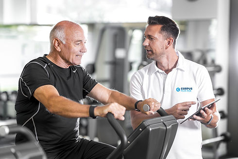 Älterer Mann auf einem Trainingsgerät mit Anweisungen von einem Trainer bei corpus plus age.