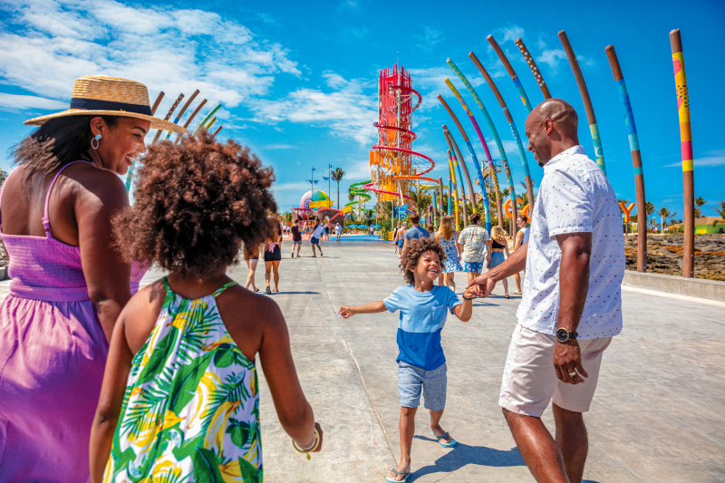 Royal Caribbean docked at at one themed water parks with a family laughing and walking toward water slides. 