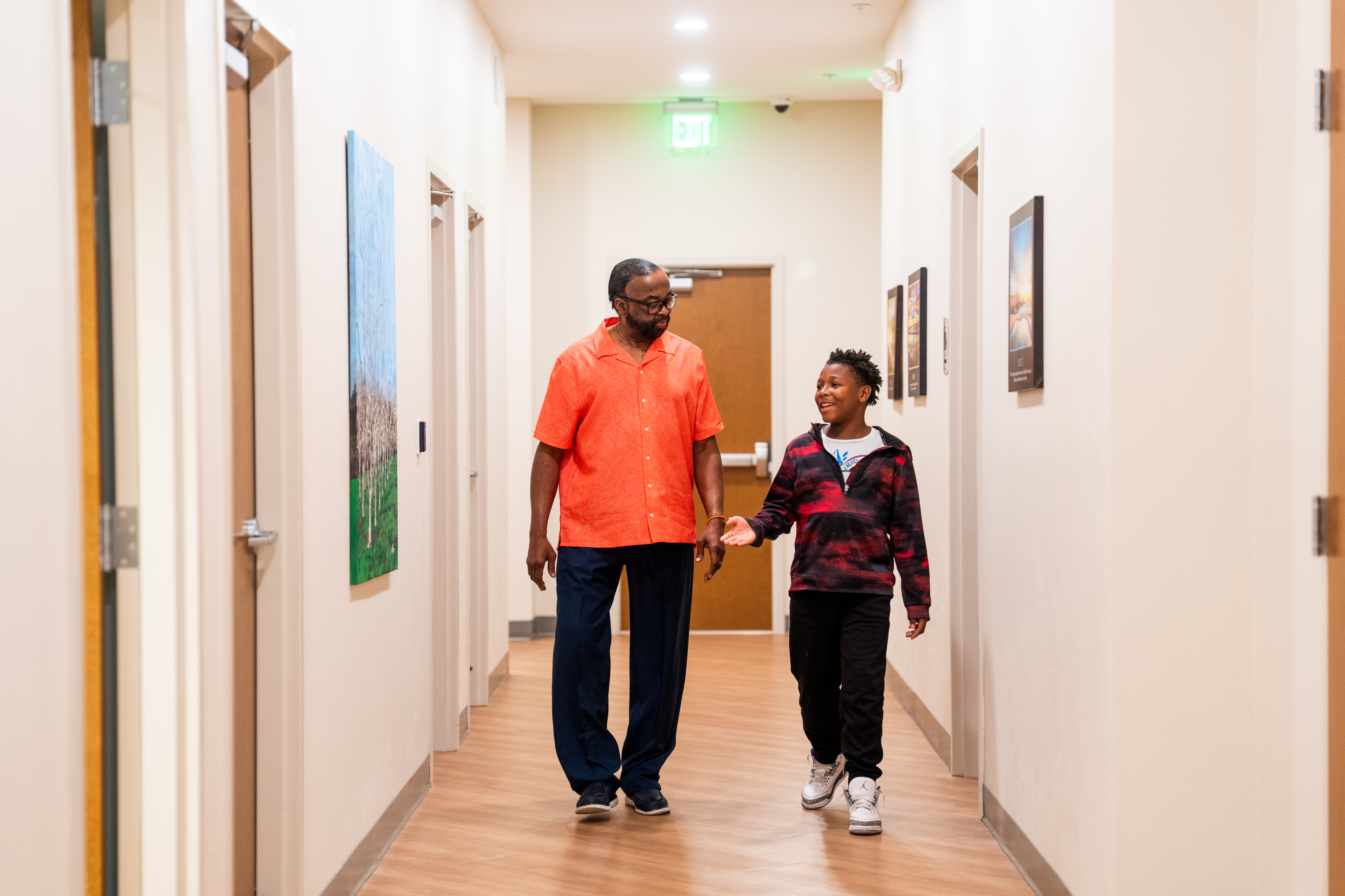 Boy speaking to man while walking down a hallway together.
