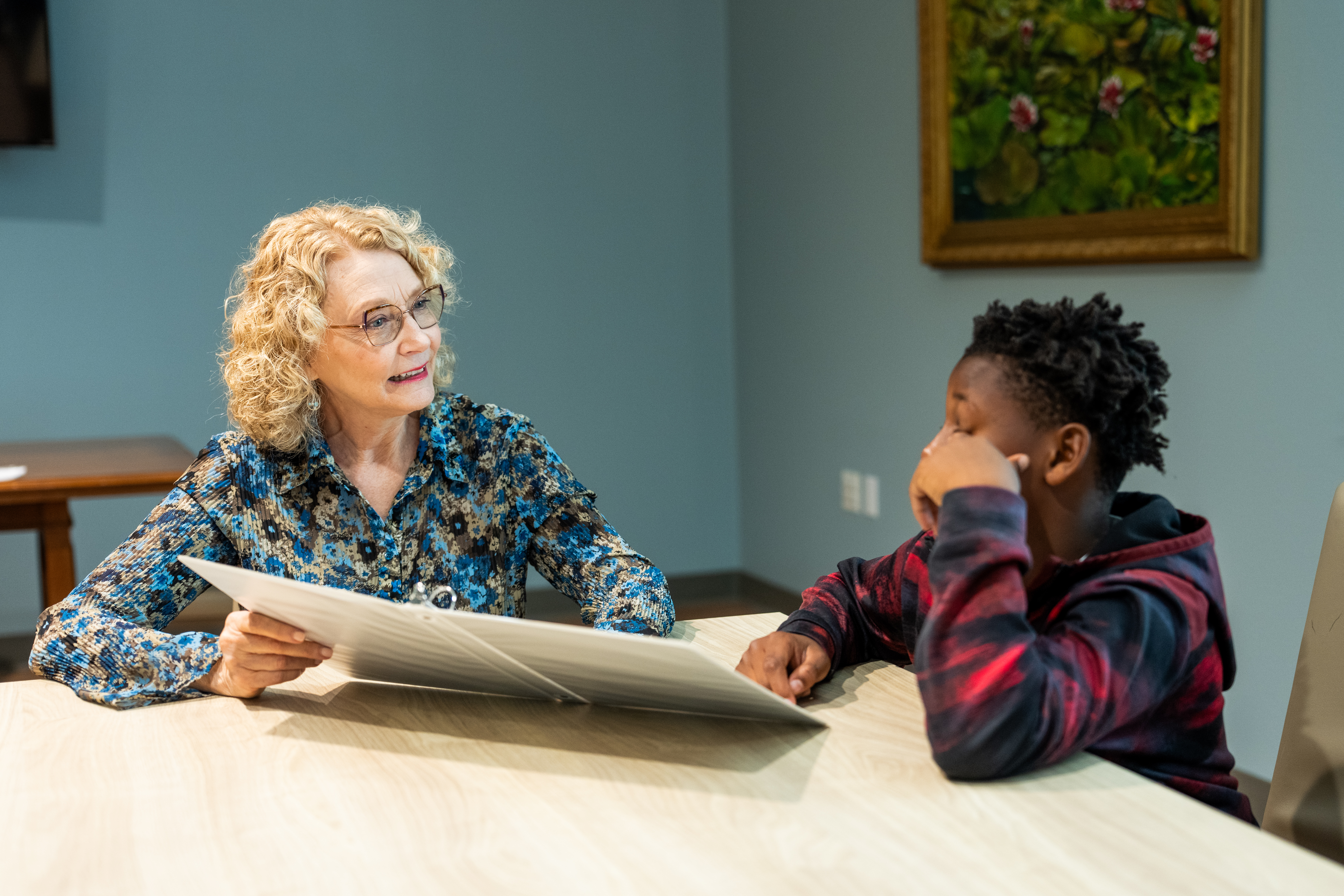 Woman helping a boy with a worksheet at a table.